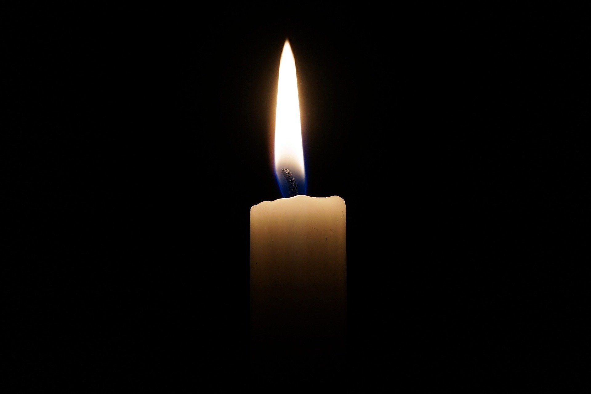 Eine Kerze brennt vor schwarzem Hintergrund.