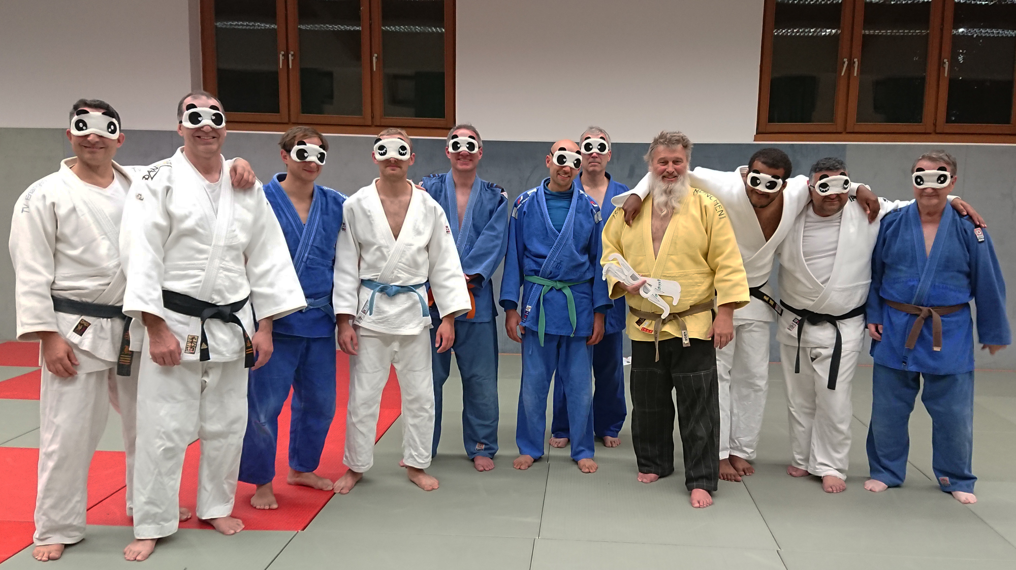 Eine Gruppe Judoka steht für ein Gruppenbild in der Halle. Alle tragen Masken über den Augen.