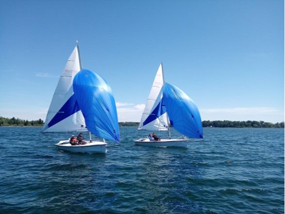 Zwei Segelboote mit jeweils zwei Segler*innen und blauer Himmel über dem See.
