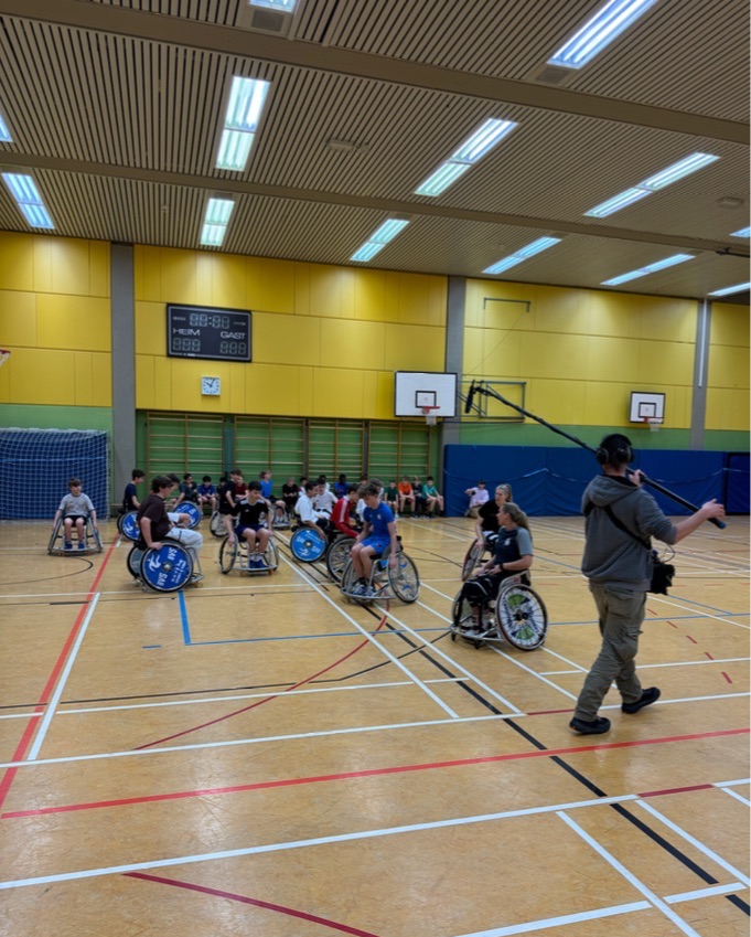 Mann mit Mikrofon nimmt Schüler beim Basketballspiel im Rollstuhl auf