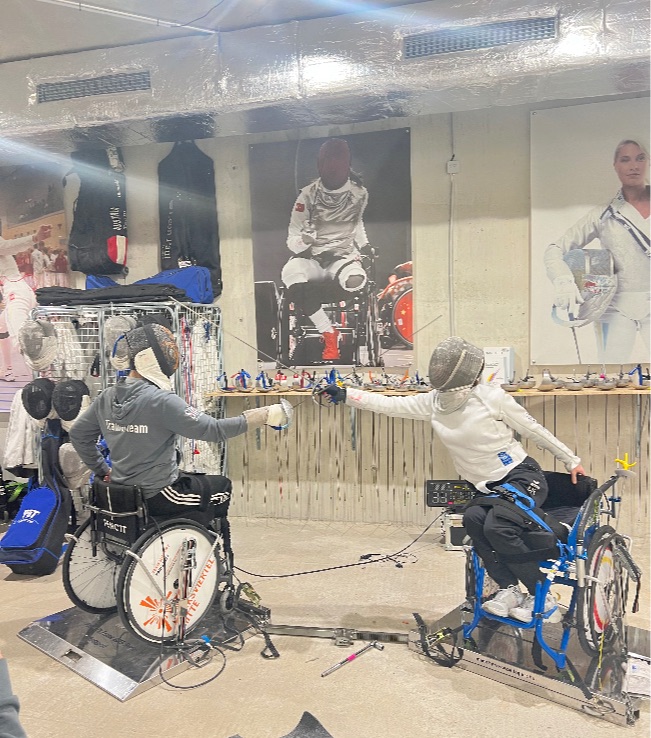 Zwei Sportler*innen in Fechtausrüstung im Rollstuhl beim Kämpfen