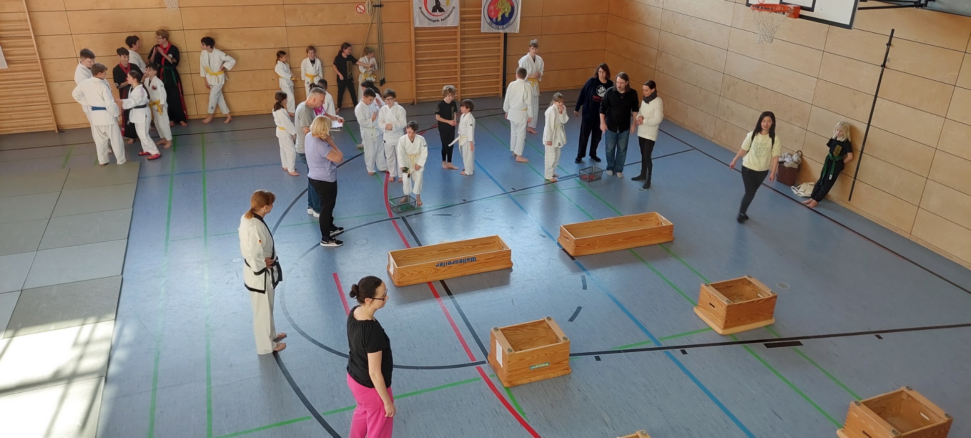 Sportgruppe Judo und Tang Soo Don in weißer Kampfkunst-Kleidung macht in einer Turnhalle Wurfübungen in Turnkästen.