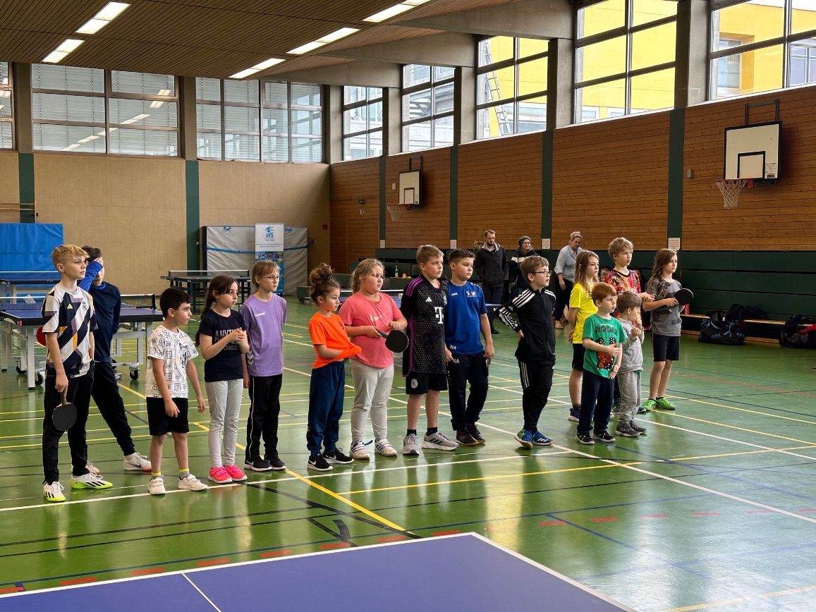 Kinder stehen nebeneinander in einer Sporthalle und halten Tischtennisschläger in der Hand